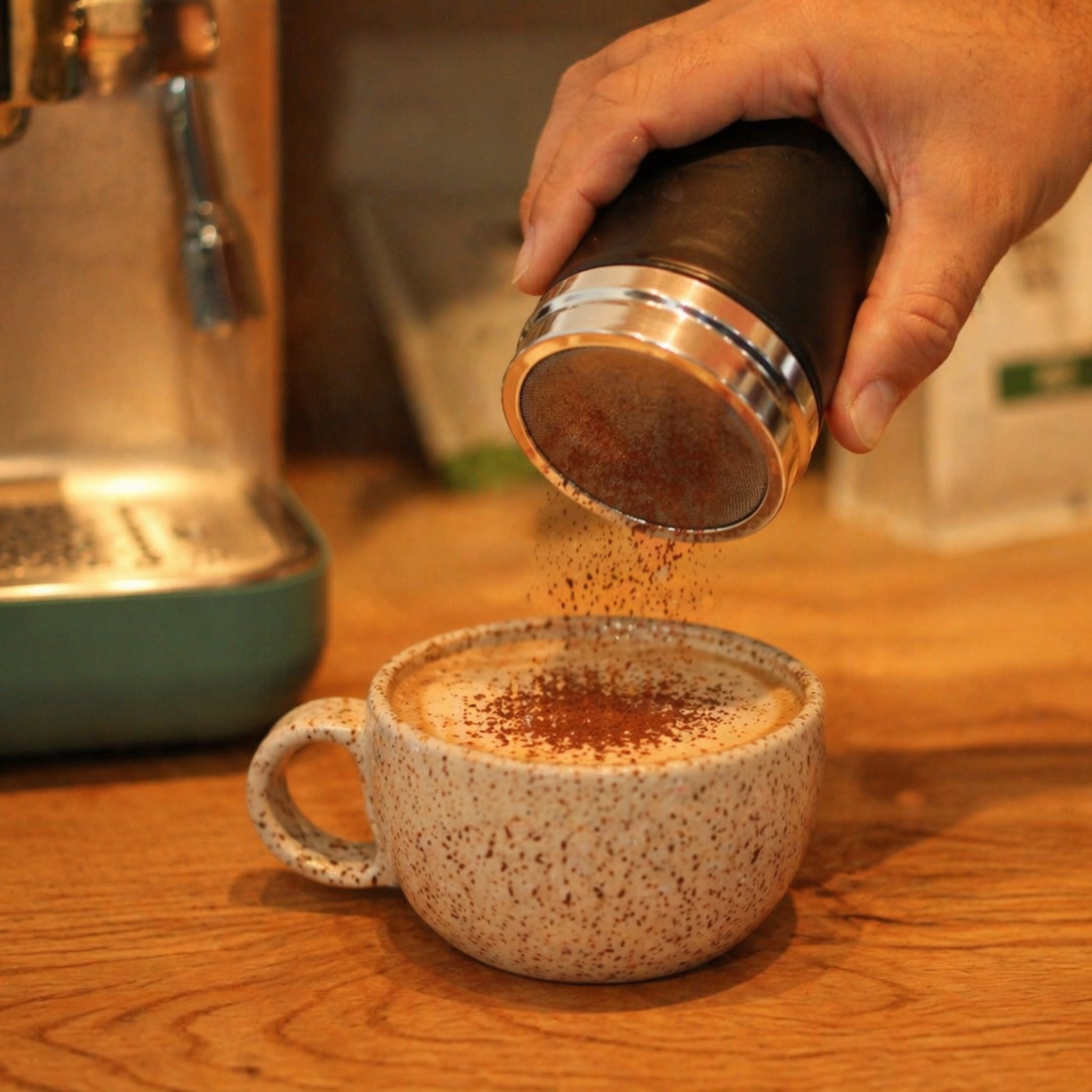 Hand sprinkling chocolate  into a cup of coffee on a wooden surface