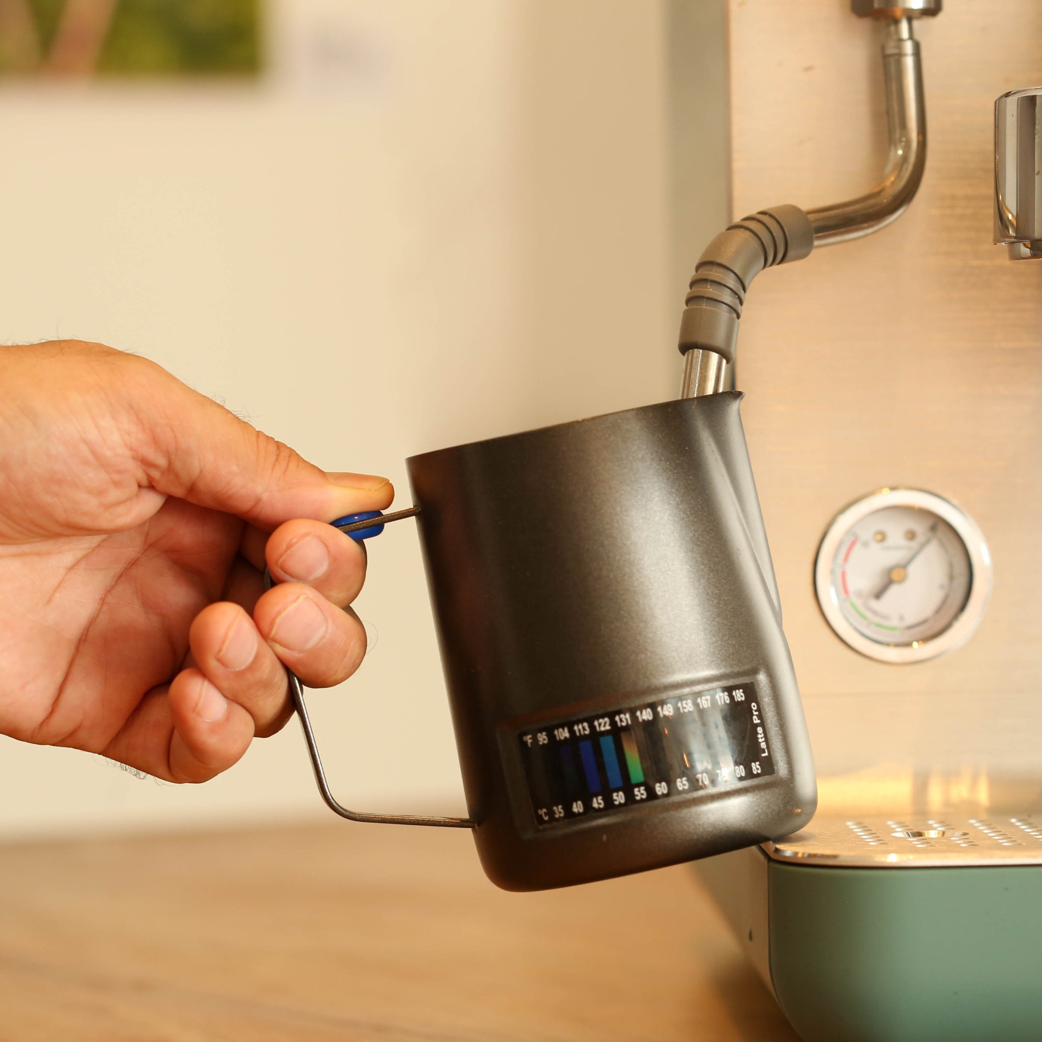 Hand holding a thermometer milk jug with a kitchen background