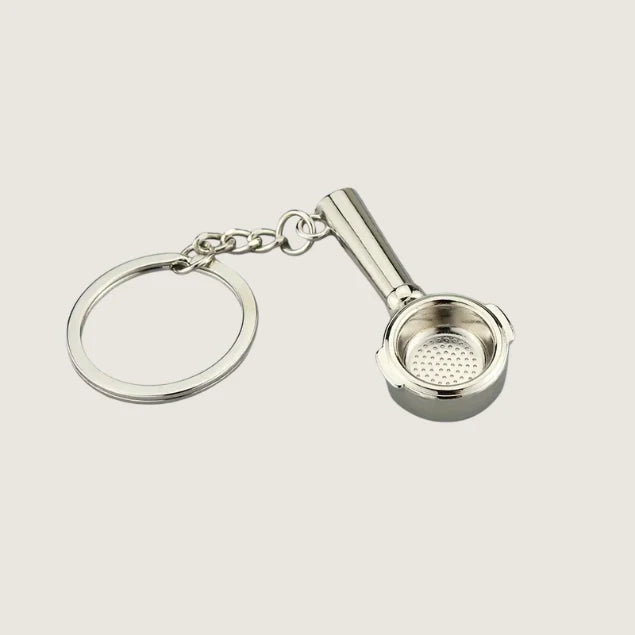 A miniature silver portafilter keychain with a detailed filter basket design, perfect for coffee lovers and baristas.