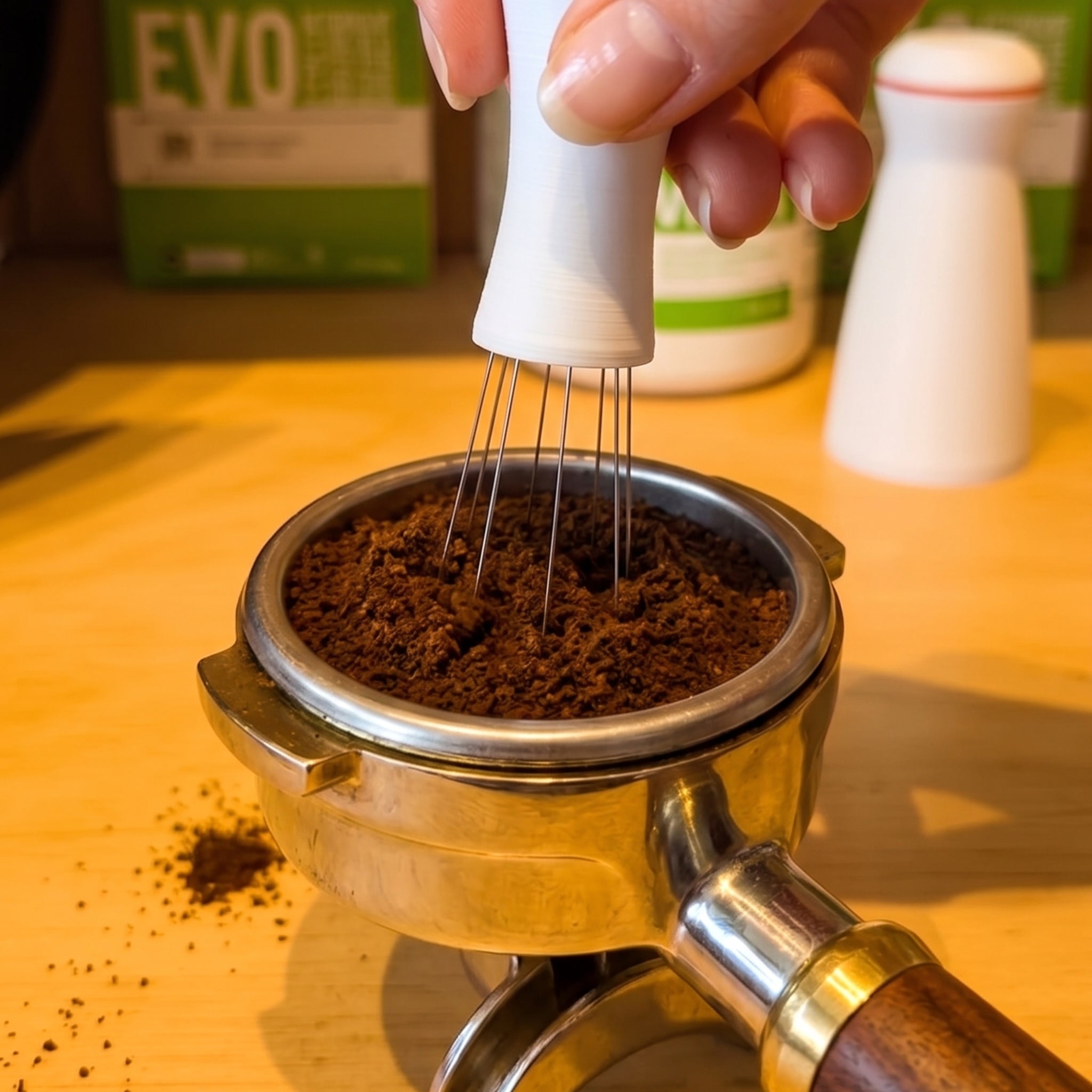Person using a whisk to mix coffee grounds in a portafilter on a wooden surface.
