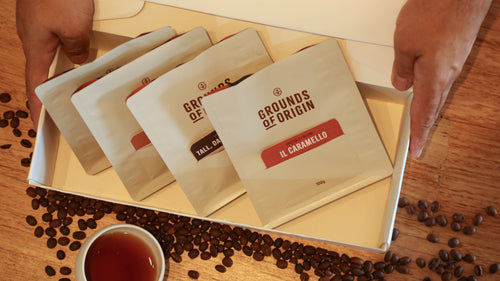 Coffee bags labeled 'Grounds of Origin' on a wooden surface with coffee beans and a cup.