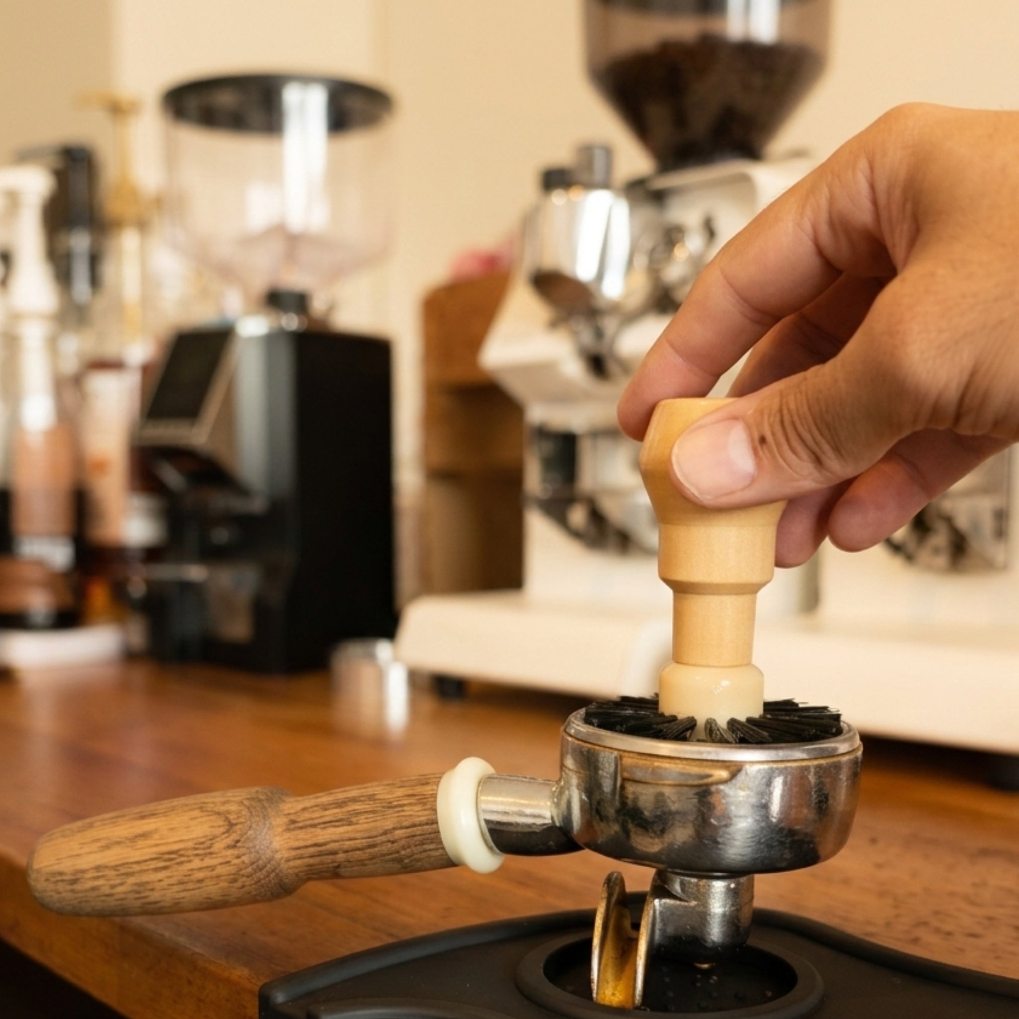 Hand using a coffee basket cleaning brush on a blurred barista station background