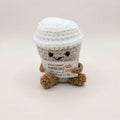 Crocheted coffee cup plush toy with a message tag on a light background