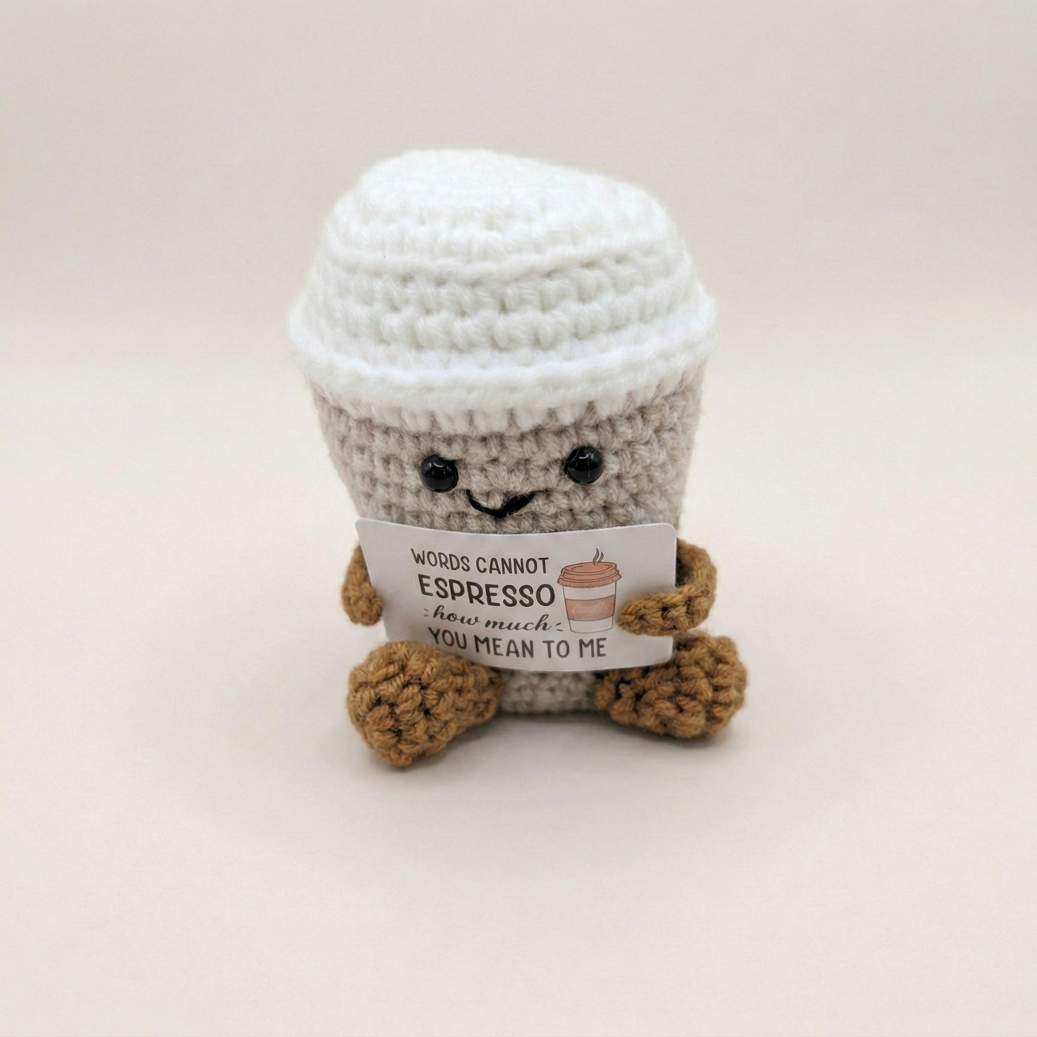 Crocheted coffee cup plush toy with a message tag on a light background
