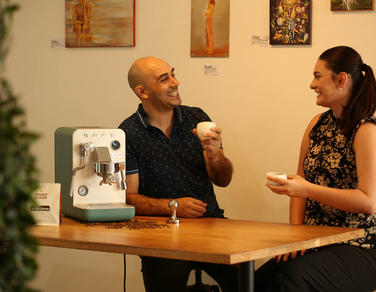 Two people enjoying coffee next to a coffee machine in Grounds of Origin Cafe