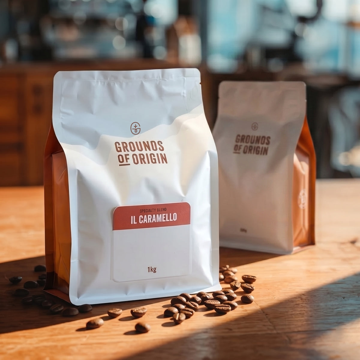 Two 'Grounds of Origin' coffee bags on a wooden table with scattered coffee beans.