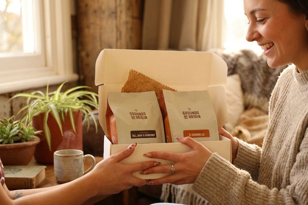 Person receiving a gift box with coffee packages from another person in a cozy indoor setting.