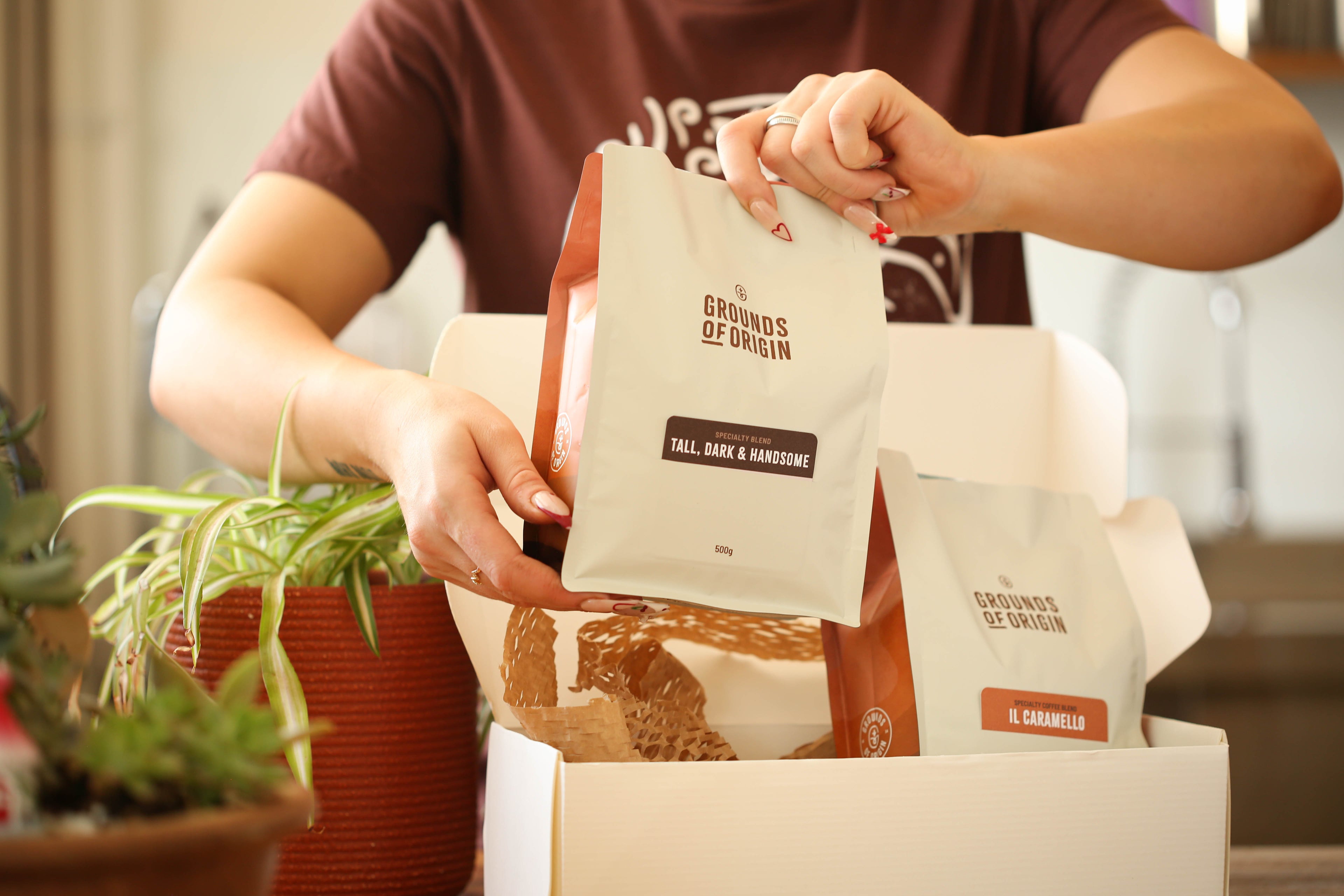 Person placing a 'Grounds of Origin' coffee bag into a box for delivery